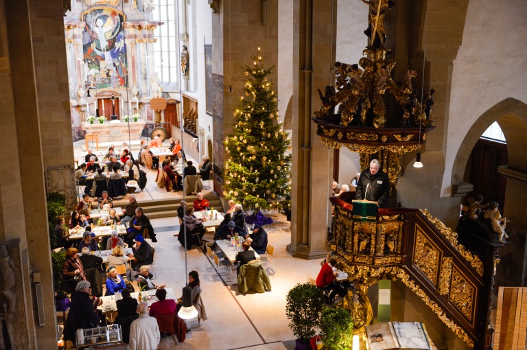 Menschen besuchen die Vesperkirche und sitzen gemeinsam an Tischen.