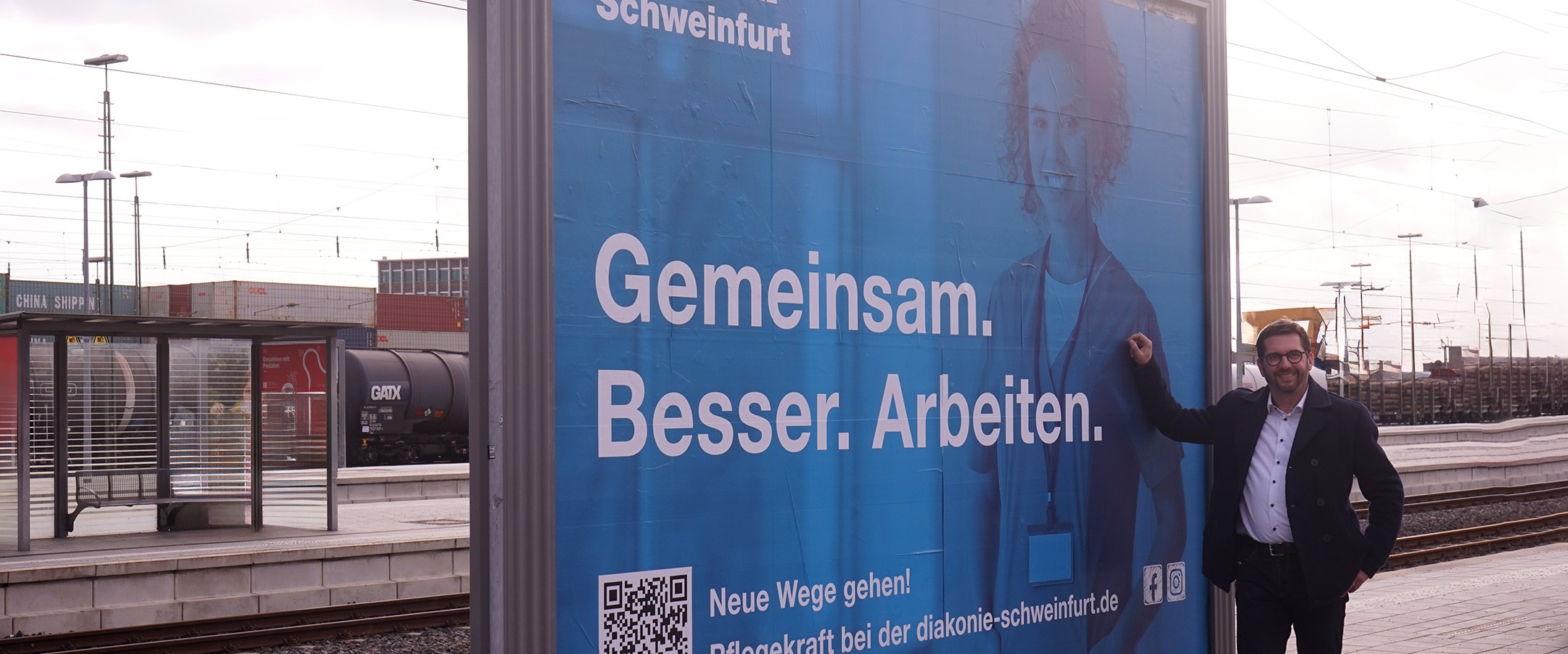 Carsten Bräuer steht vor Plakate mit der Ausschrift Gemeinsam besser Arbeiten