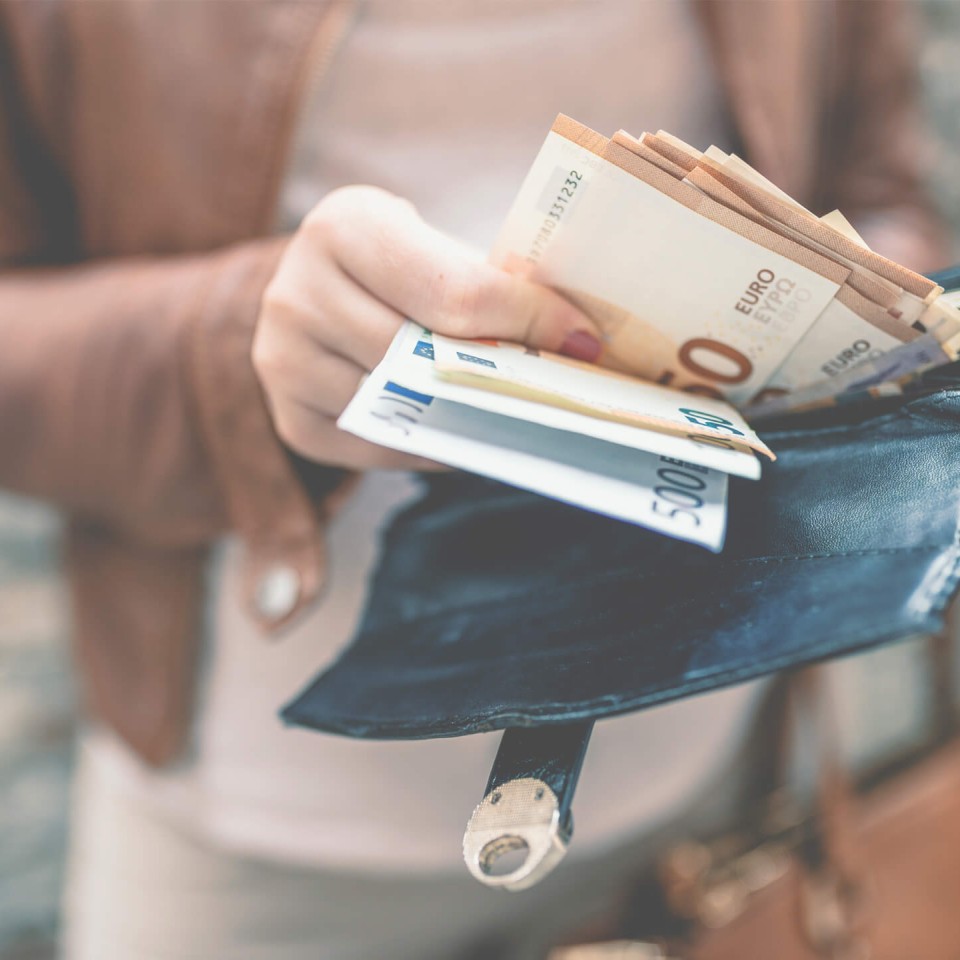 Eine Person hält eine Geldbörse in der Hand und zählt mehrere Euro-Geldscheine.