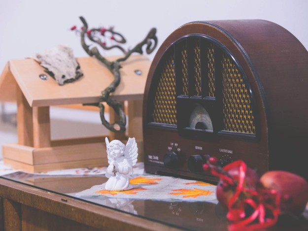 Ein altes Radio mit Holzkorpus steht auf einem Tisch, daneben ein kleines weißes Engel-Figur und ein Vogelhaus.