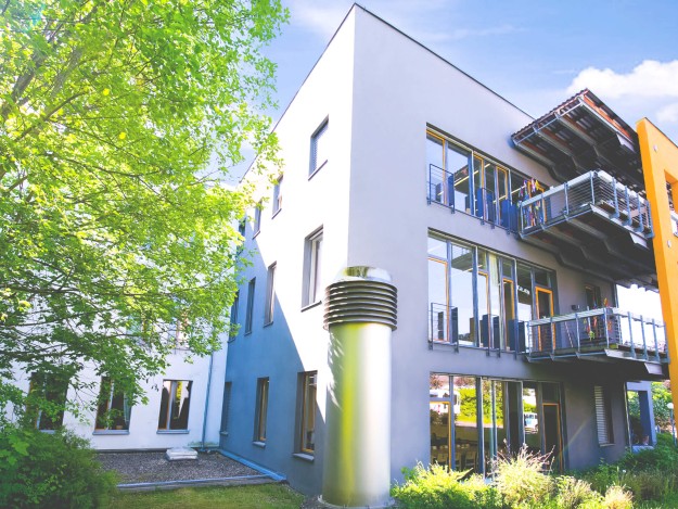 Viel Licht fällt auf ein großes Gebäude mit schöner Gartenanlage.
