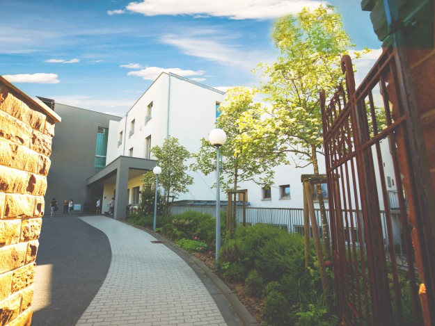 Großes modernes Gebäude umgeben von Bäumen und Gartenanlage.