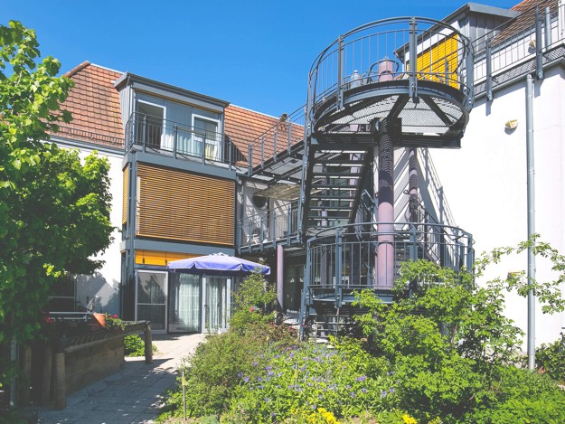 Rückseite eines Gebäudes mit Treppenaufgang und blühendem Garten.
