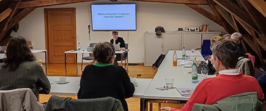 Angehörigenschulung "Hilfe beim Helfen" Personen sitzen an Tischen mit Blick auf eine Präsentation