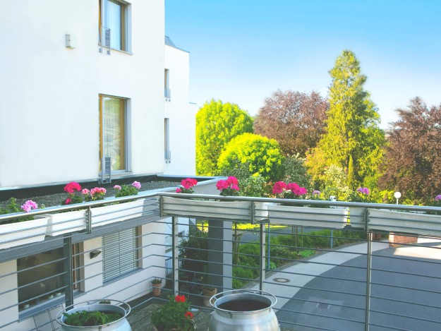 Balkon mit farbenfrohen Blumen und Blick auf einen Garten.