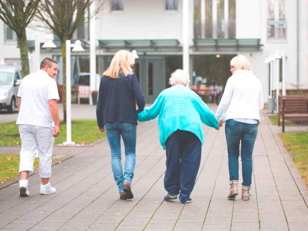 Eine Pflegekraft, zwei Angehörige und eine ältere Dame gehen auf das Pflegezentrum Maininsel zu