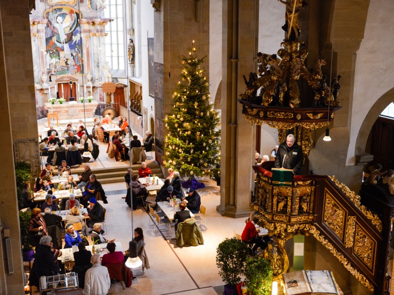 Menschen besuchen die Vesperkirche und sitzen gemeinsam an Tischen.
