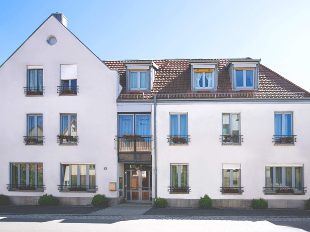 Fassade eines dreistöckigen Gebäudes mit Balkonen und Blumentöpfen.